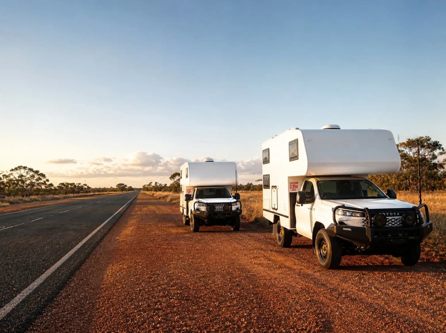 Two matching single-cab utilities with white camper bodies, parked beside a remote highway