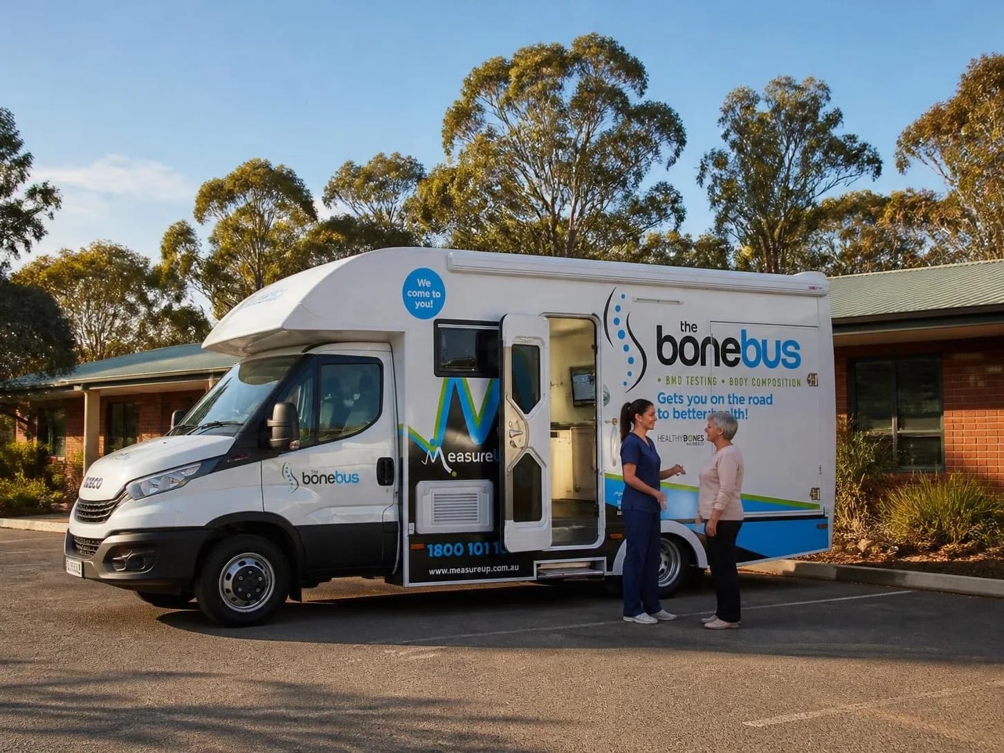 Mobile medical unit in operator livery with the side door open, parked outside a clinic